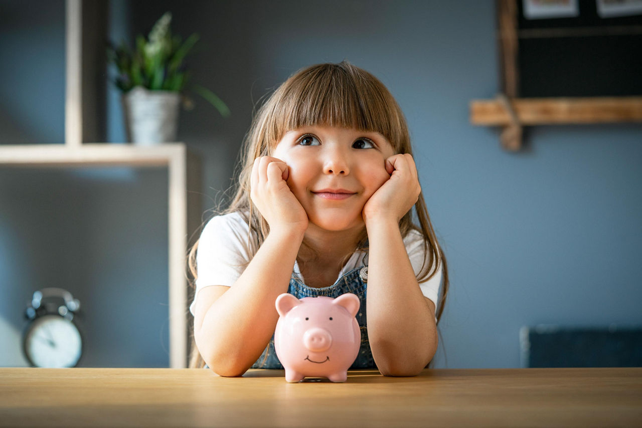 Mädchen an einem Tisch mit einem Sparschwein vor sich