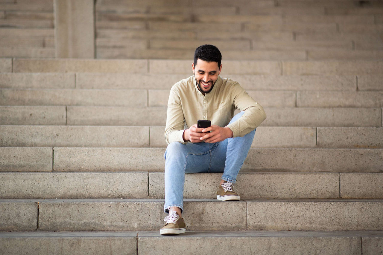 Mann sitzt lachend mit Smartphone auf Stufen