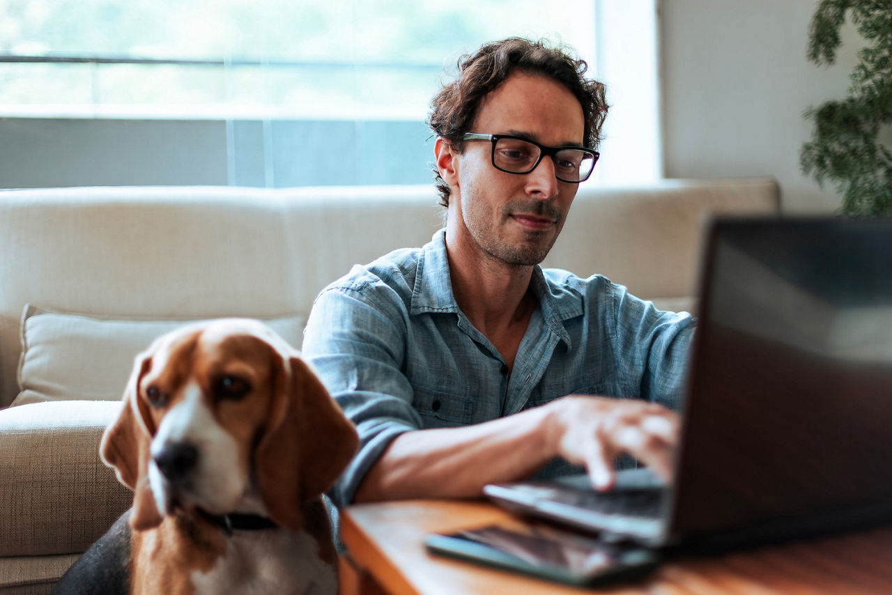 Mann mit Hund arbeitet an einem Laptop