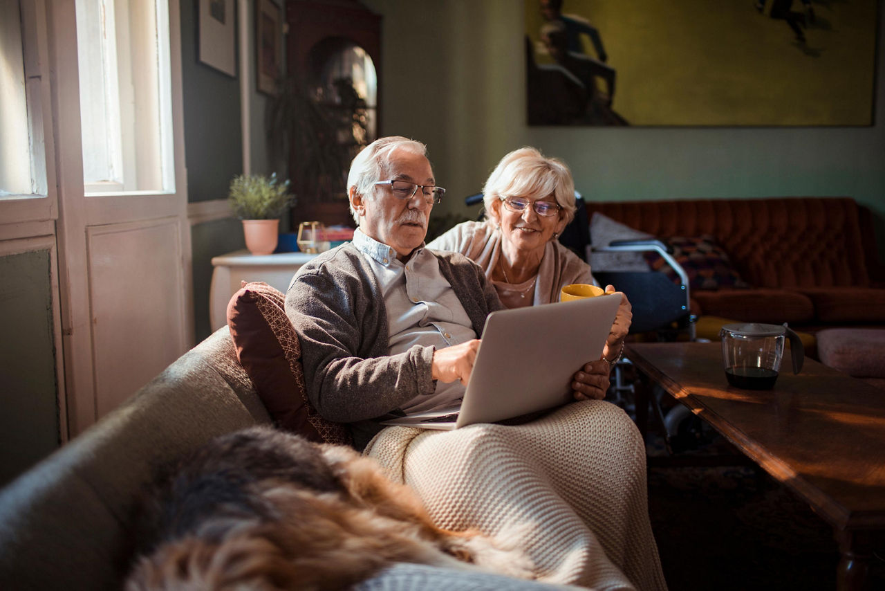 Älteres Paar schaut auf der Couch in einen Laptop