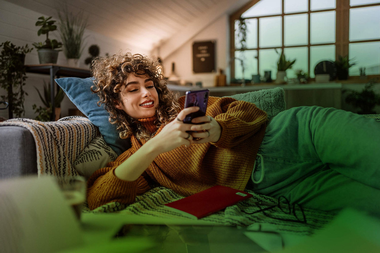 Frau liegt auf der Couch und schaut aufs Smartphone