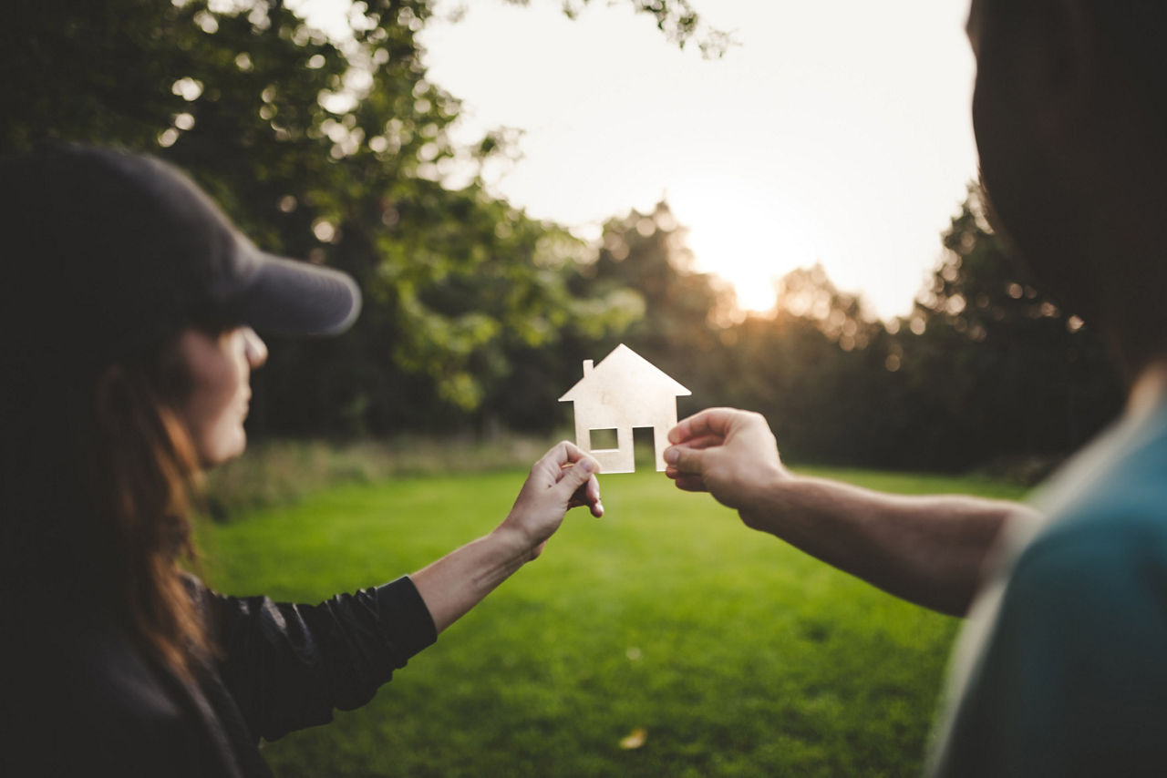 Zwei Menschen halten ein Haus aus Papier in die Natur