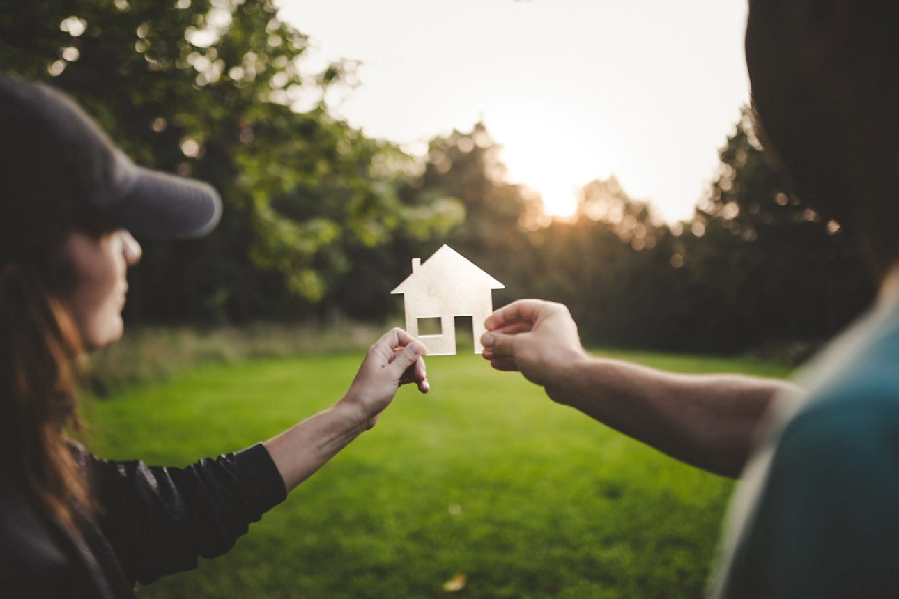 Zwei Menschen halten ein Haus aus Papier in die Natur