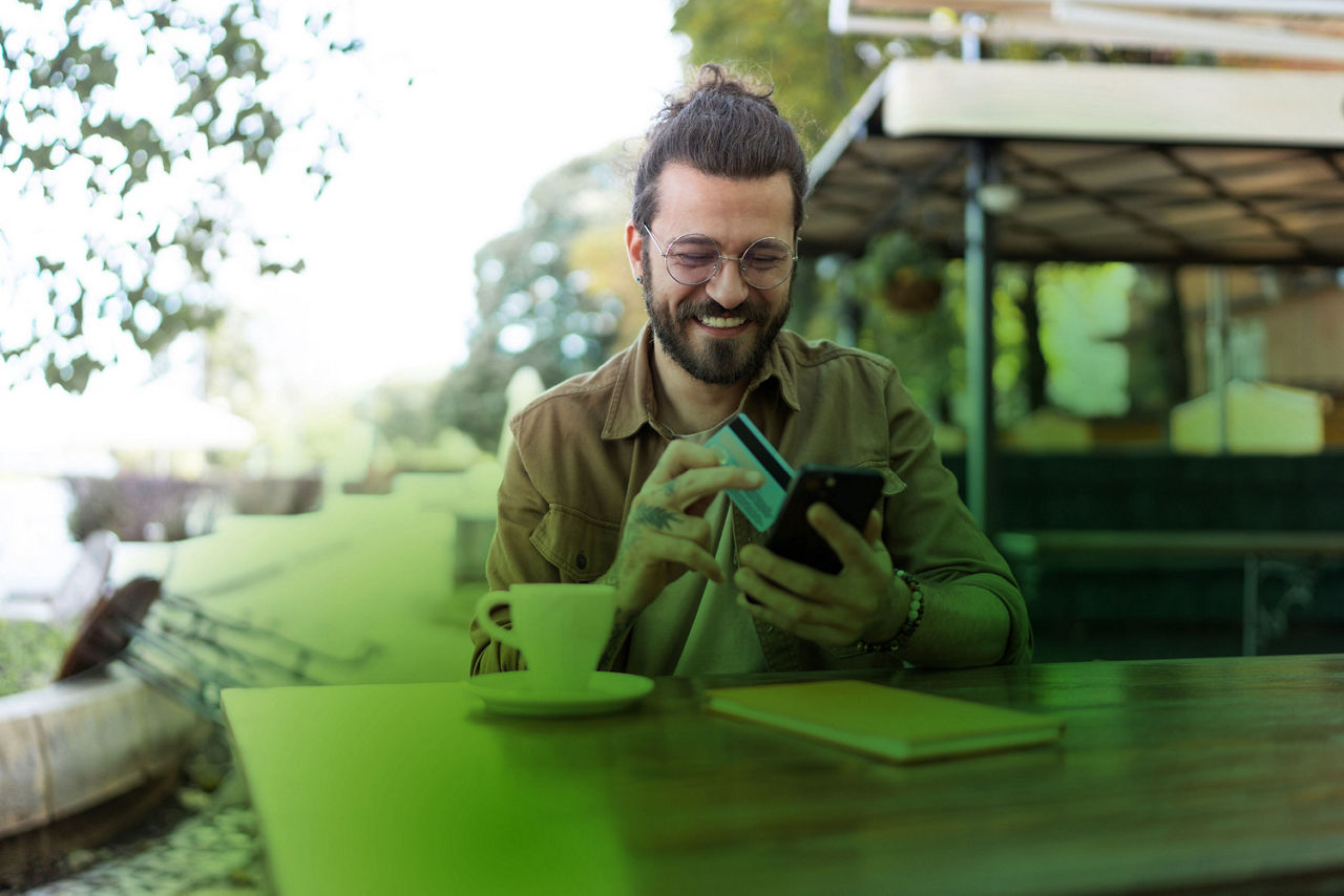Mann mit Kreditkarte und Handy in der Hand sitzt im Café