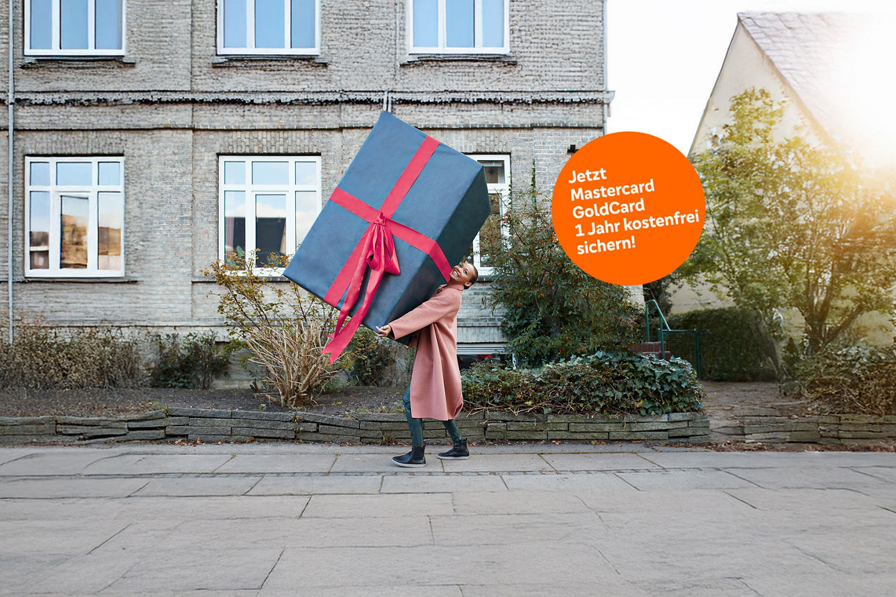 Junge Frau in rosafarbenem Wollmantel trägt ein übergroßes Paket mit roter Schleife