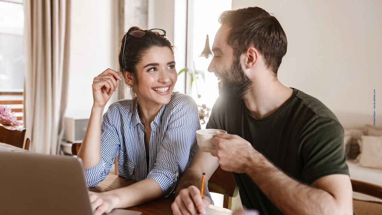 ein Mann und eine Frau sitzen lachend und erfreut  vor dem Computer