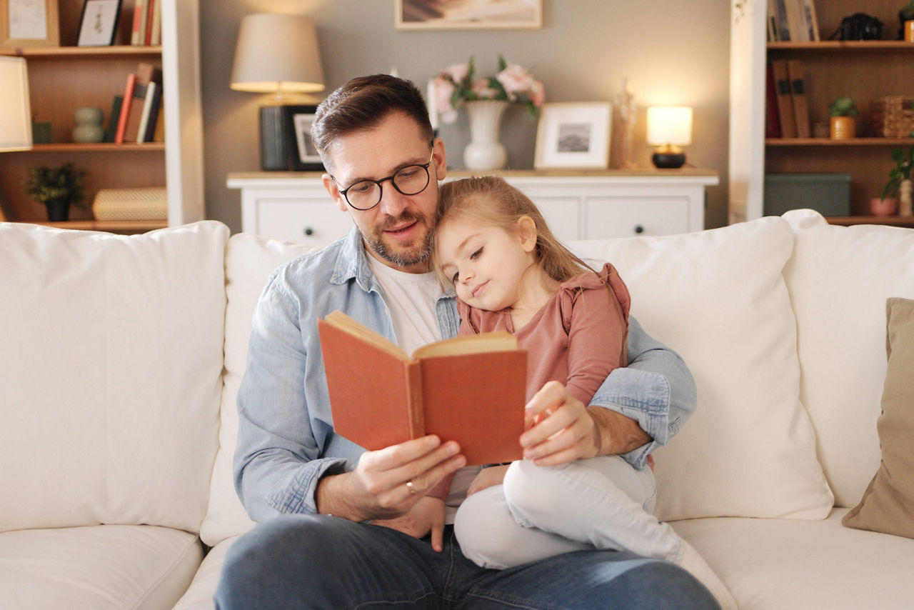 Vater liest seiner jungen Tochter ein Buch vor während sie auf dem Sofa entspannen