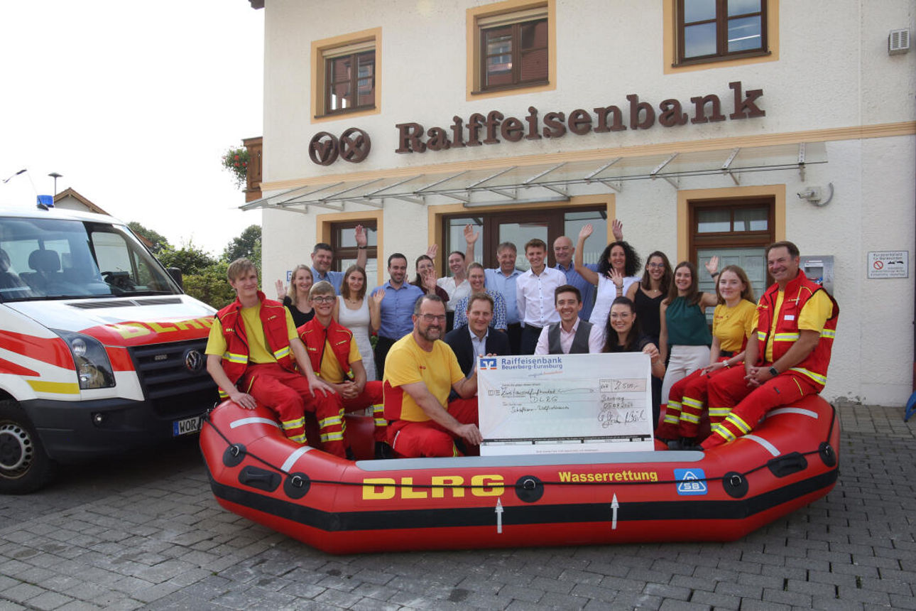 Gruppe von Menschen, darunter Mitglieder eines Wasserrettungsteams, stehen vor einer Raiffeisenbank 