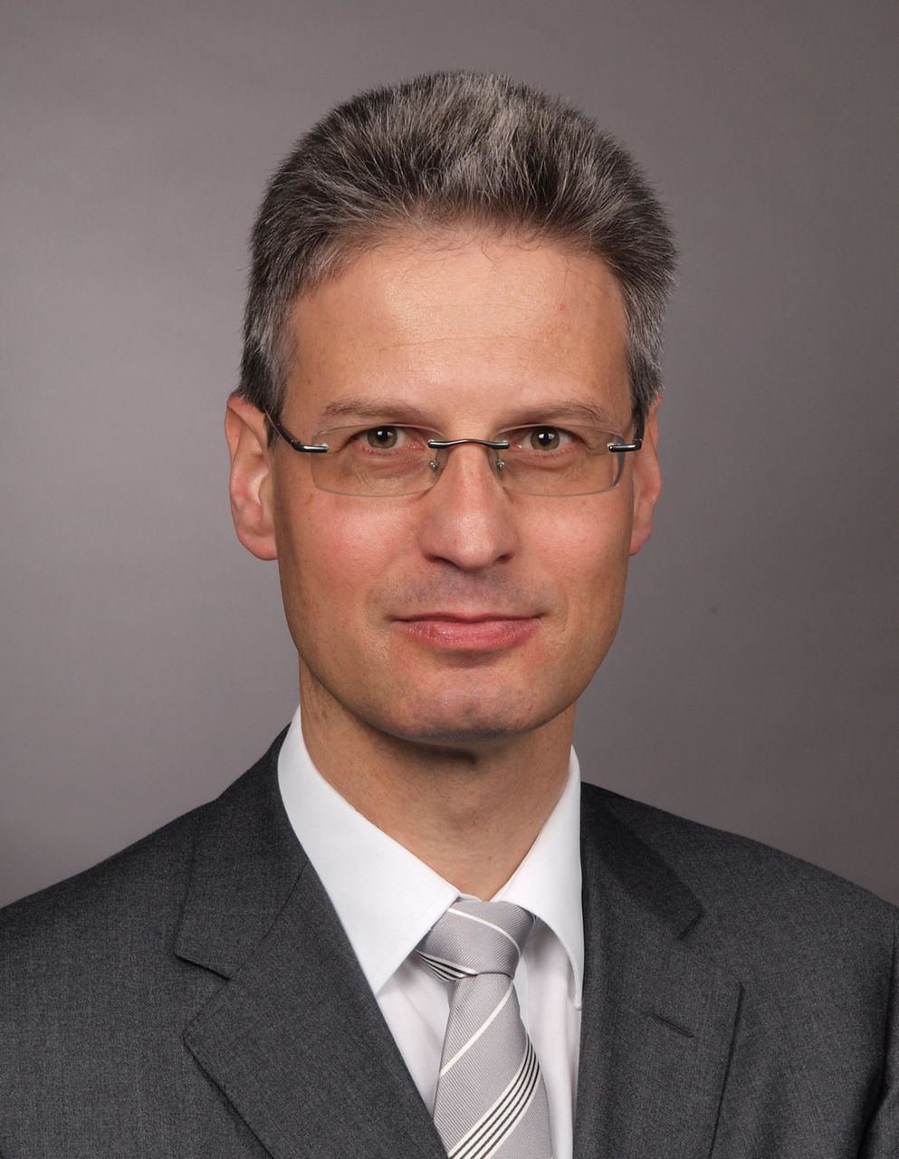 Mitarbeiter der Bank im Anzug mit grauer Krawatte lächelt in die Kamera.