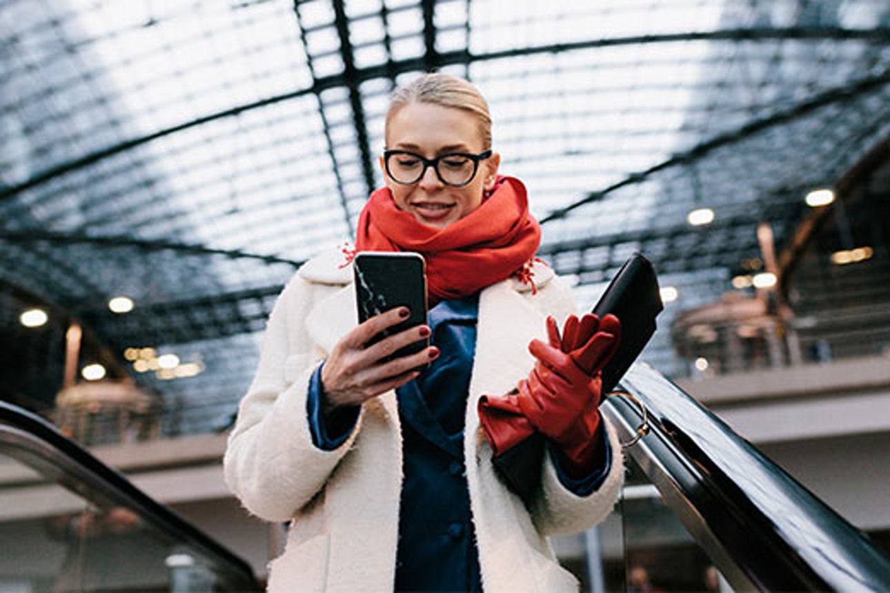 Junge Frau mit Smartphone auf einer Rolltreppe