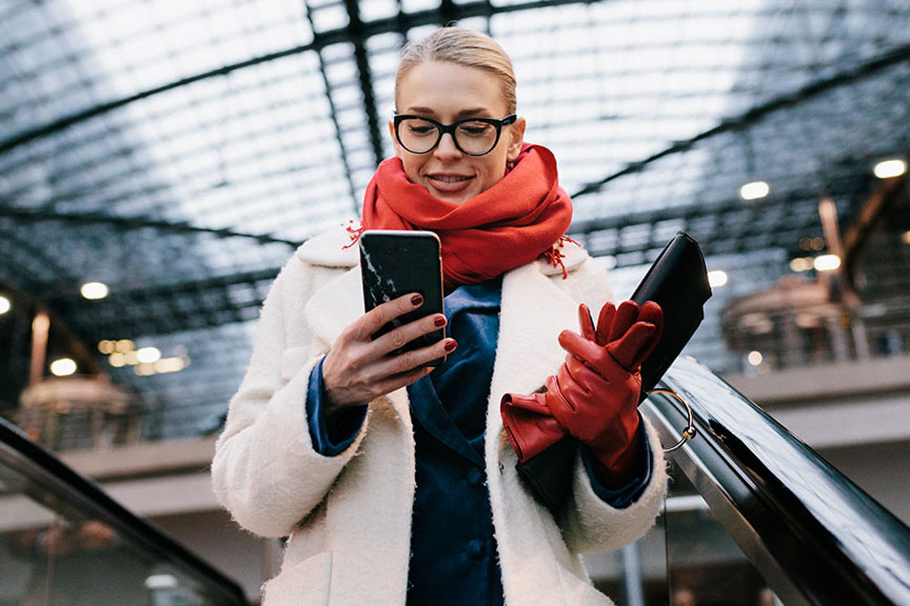 Frau auf Rolltreppe mit Smartphone in der Hand