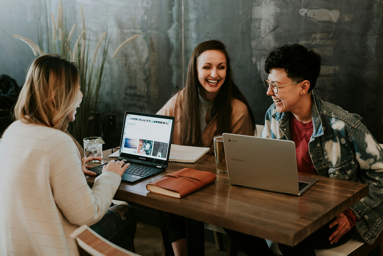 Drei junge Frauen sitzen im Café an einem Tisch und arbeiten an ihren Notebooks