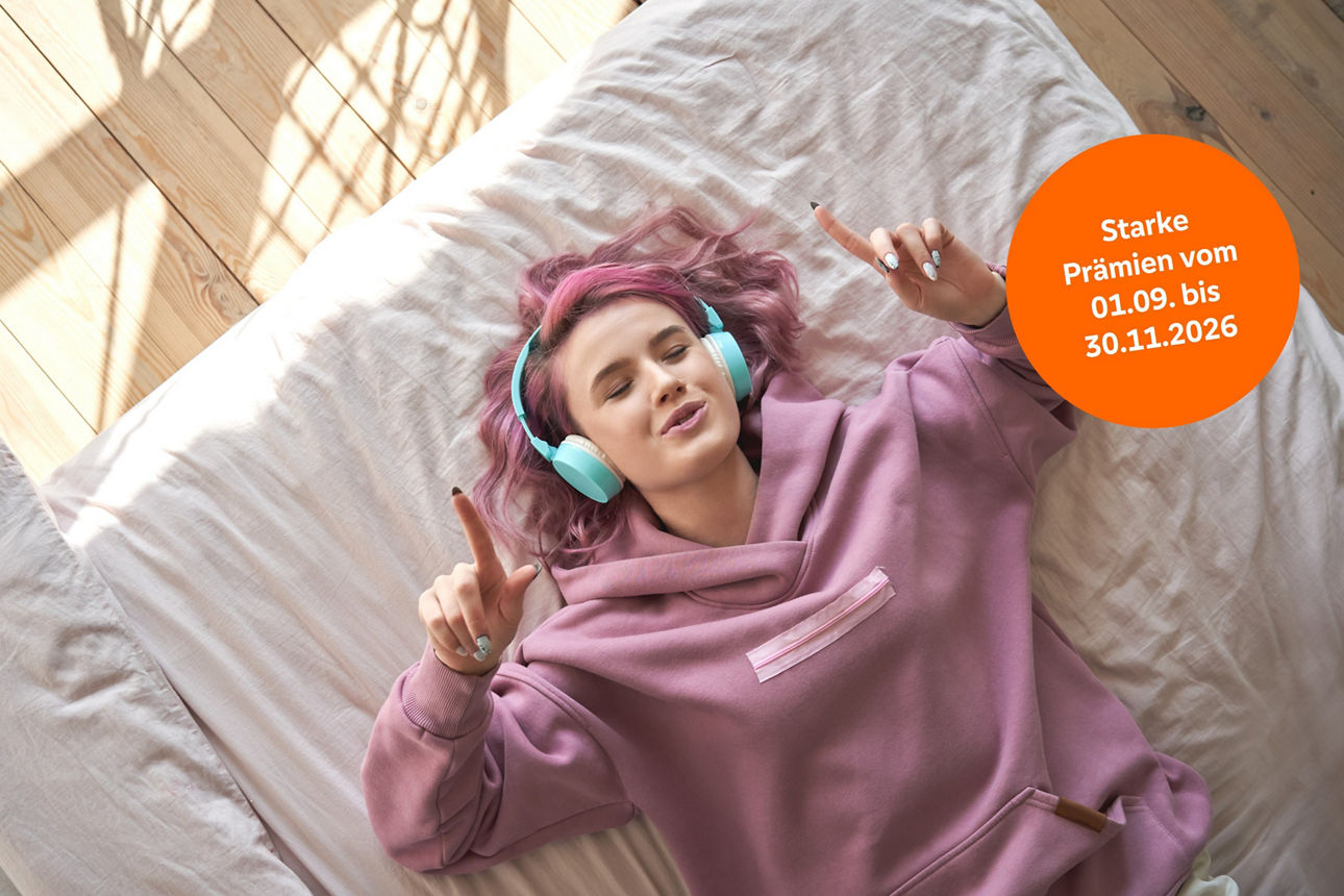 Happy funny teen girl with pink hair wear headphones lying in comfortable bed listening new pop music enjoying singing song with eyes closed relaxing in cozy bedroom at home. Top view from above.