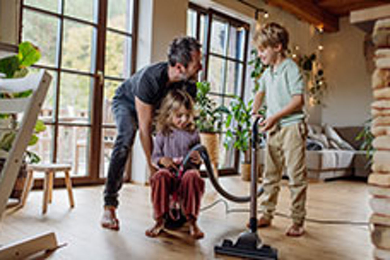 Eine schwangere Frau mit einem Pinsel in der Hand steht lächelnd vor einem Holzhaus. Bausparen mit Bausparvertrag