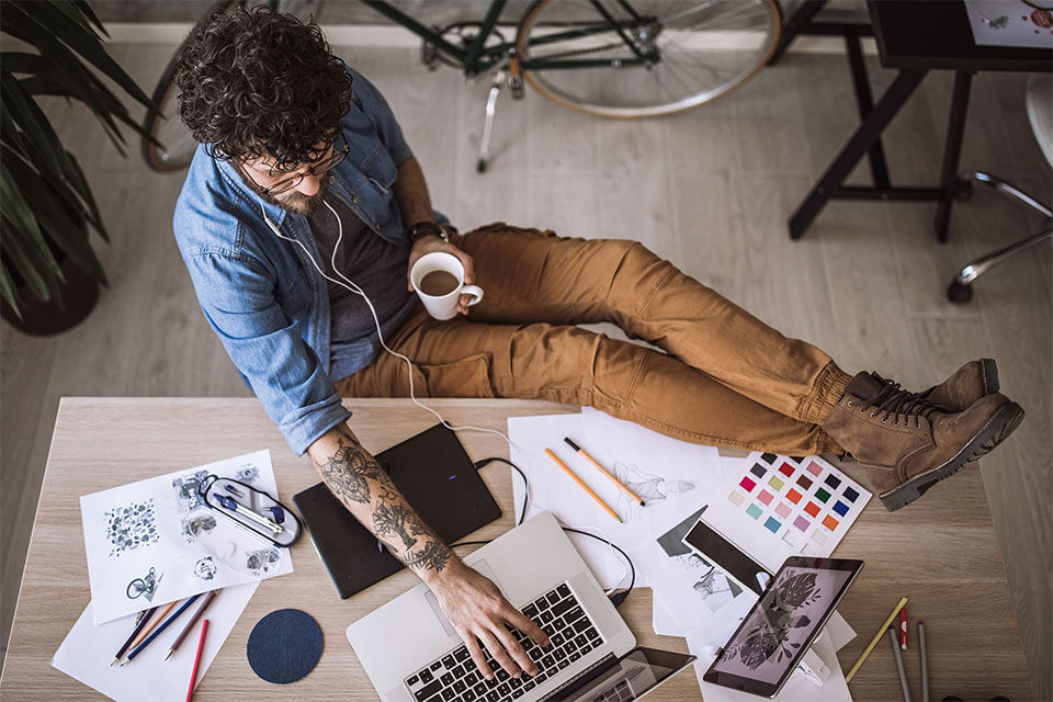 Designer arbeitet gelassen am Schreibtisch mit Kaffee und Kopfhörern