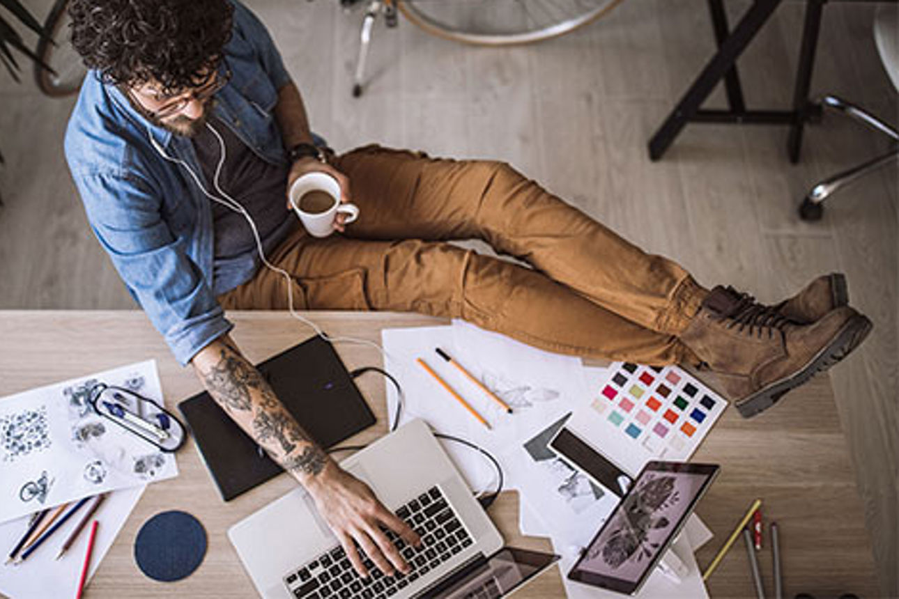 Designer arbeitet gelassen am Schreibtisch mit Kaffee und Kopfhörern