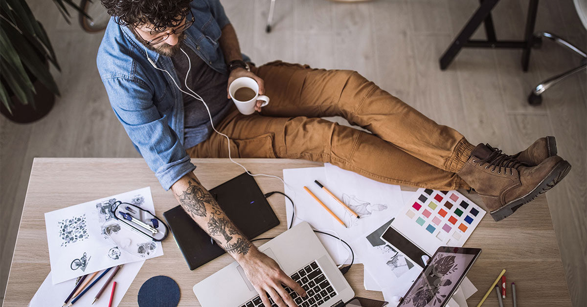 Designer arbeitet gelassen am Schreibtisch mit Kaffee und Kopfhörern