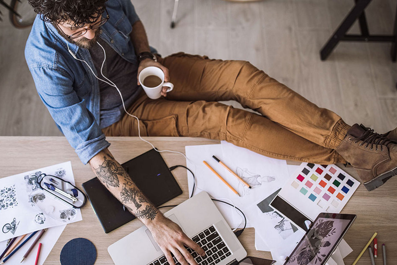 Designer arbeitet gelassen am Schreibtisch mit Kaffee und Kopfhörern