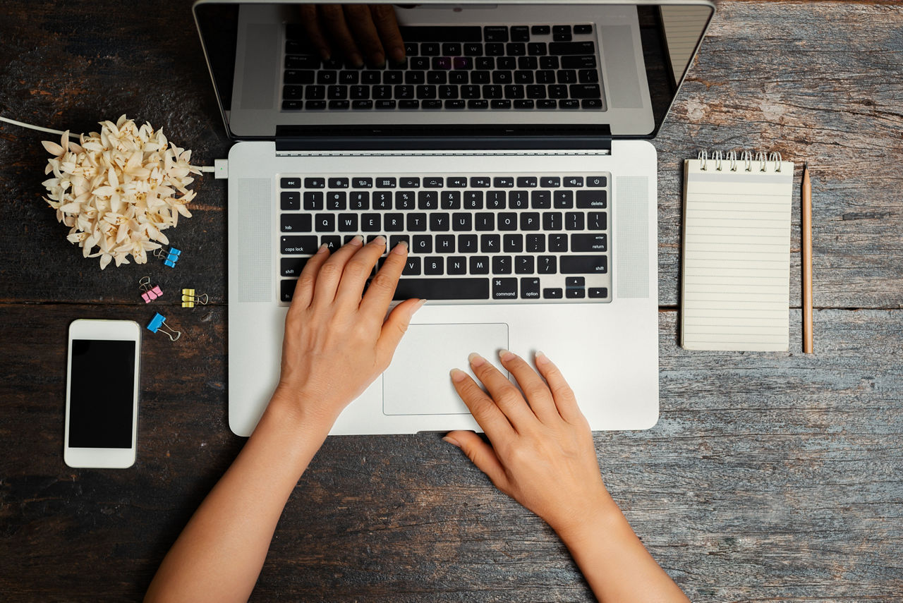 Nahaufnahme von oben der Hände einer Geschäftsfrau die an einem Laptop arbeitet mit einem Smartphone auf einem Vintage-Holzti