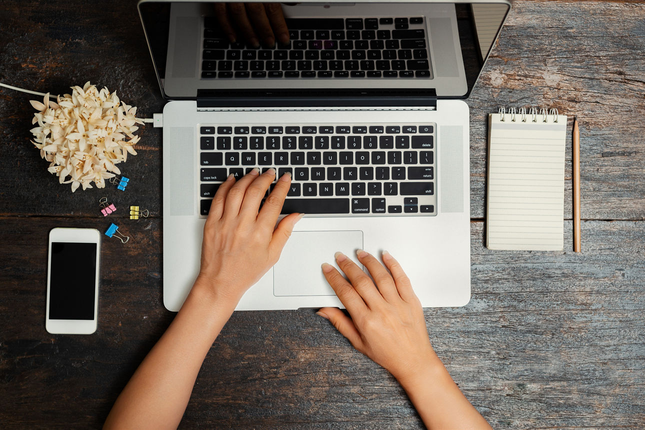 Nahaufnahme von oben der Hände einer Geschäftsfrau die an einem Laptop arbeitet mit einem Smartphone auf einem Vintage-Holzti
