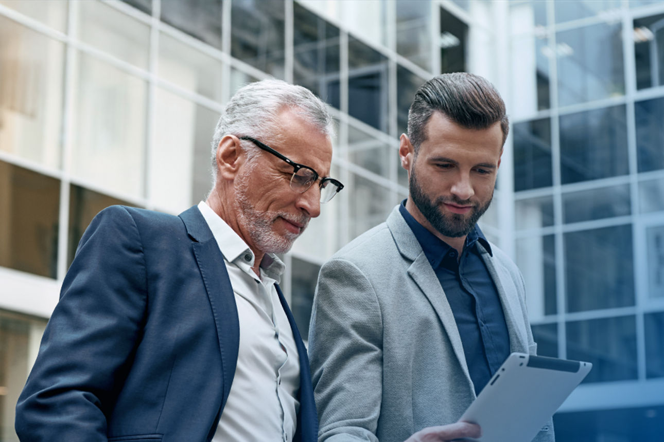 Zwei Männer vor einem Hochhaus blicken gemeinsam auf ein Tablet