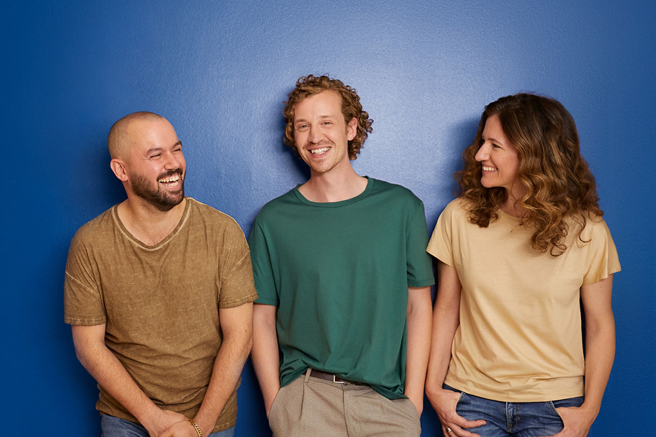 Drei Menschen stehen vor einer blauen Wand und lachen