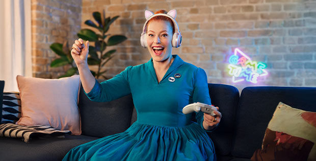 Frau mit Controller im Kleid auf dem Sofa.