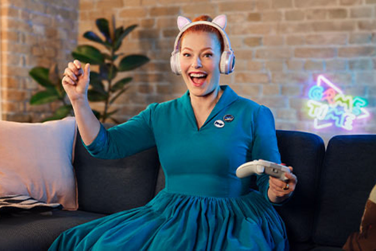 Frau mit Controller im Kleid auf dem Sofa.