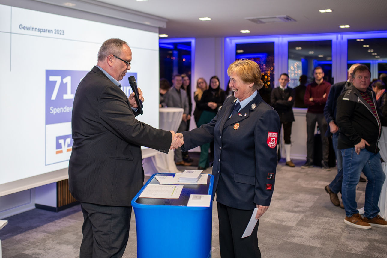 Mann mit Mikrofon und schüttelt Frau in Uniform die Hand