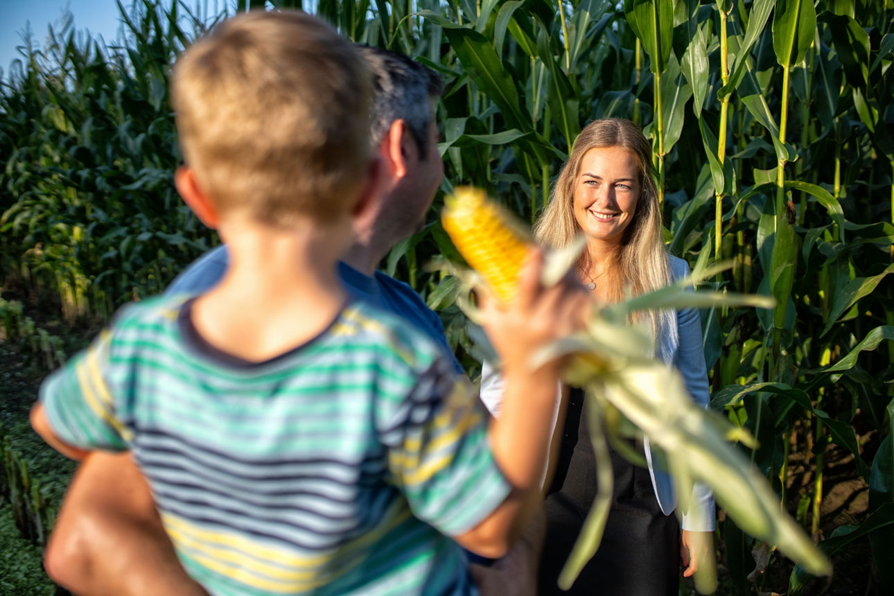 Agrarkundenbetreuerin steht mit ihrem Kunden auf einem Maisfeld.