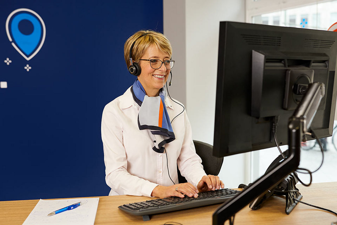 Beraterin mit Headset vor einem Computer in einer Bankfiliale