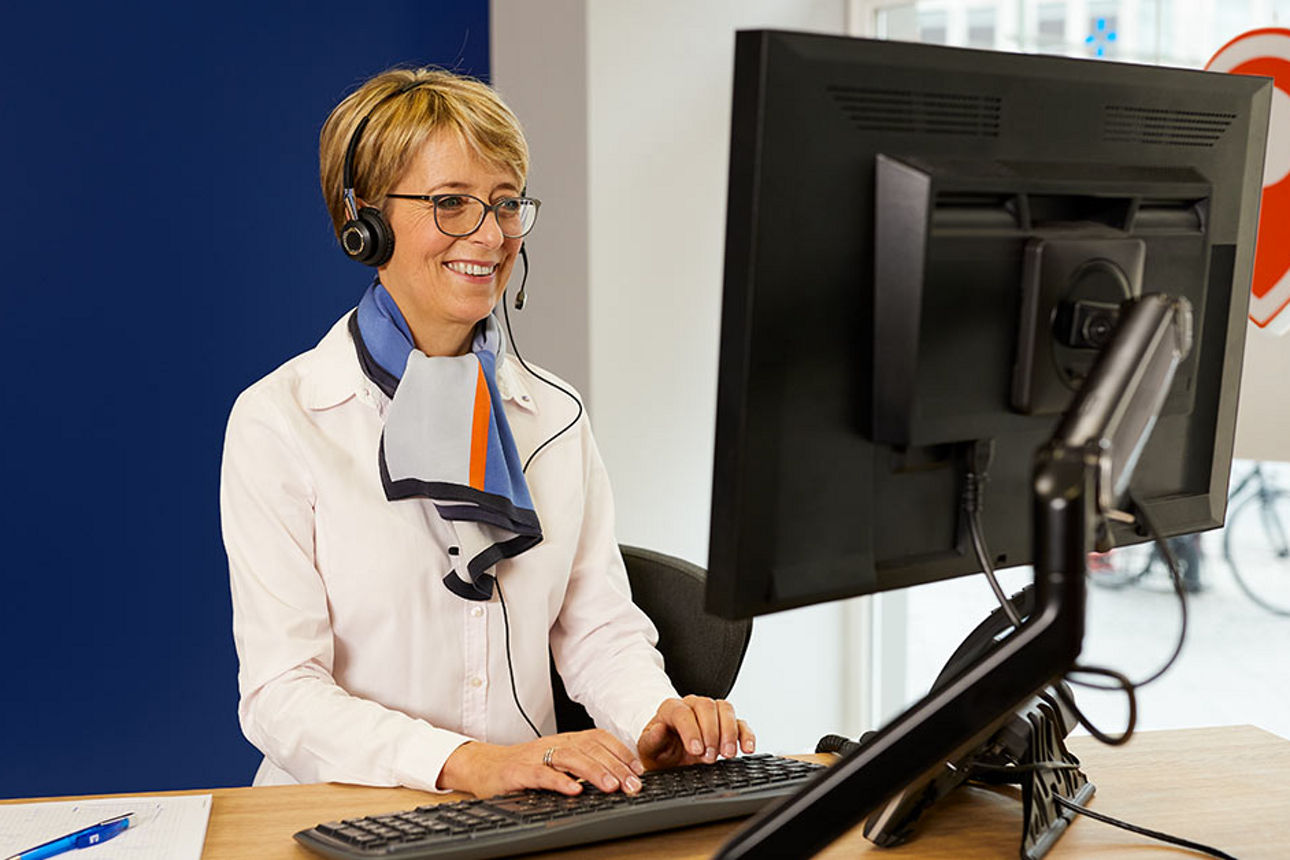 Beraterin mit Headset vor einem Computer in einer Bankfiliale.