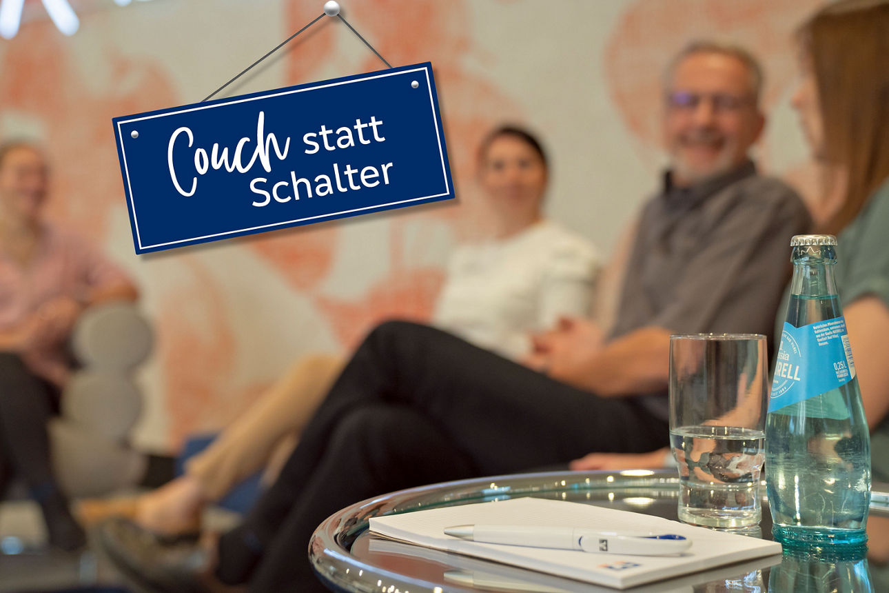 Menschen auf einer Couch, im Vordergrund ein Tischchen mit Notizblock, Stift und Wasserflasche