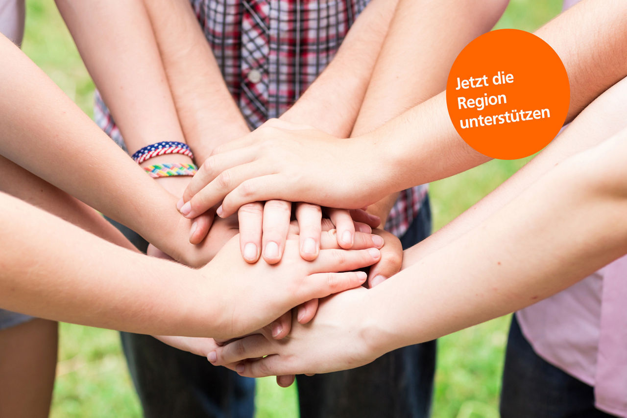 Teilweise sichbare Menschen, die im Kreis stehen und die Hände in der Mitte übereinander legen. 