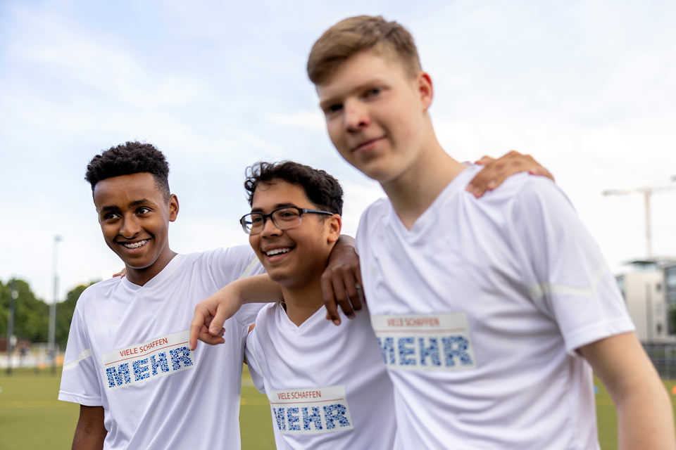 Drei junge Fußballspieler mit dem „Viele schaffen mehr“-Logo auf den Trikots