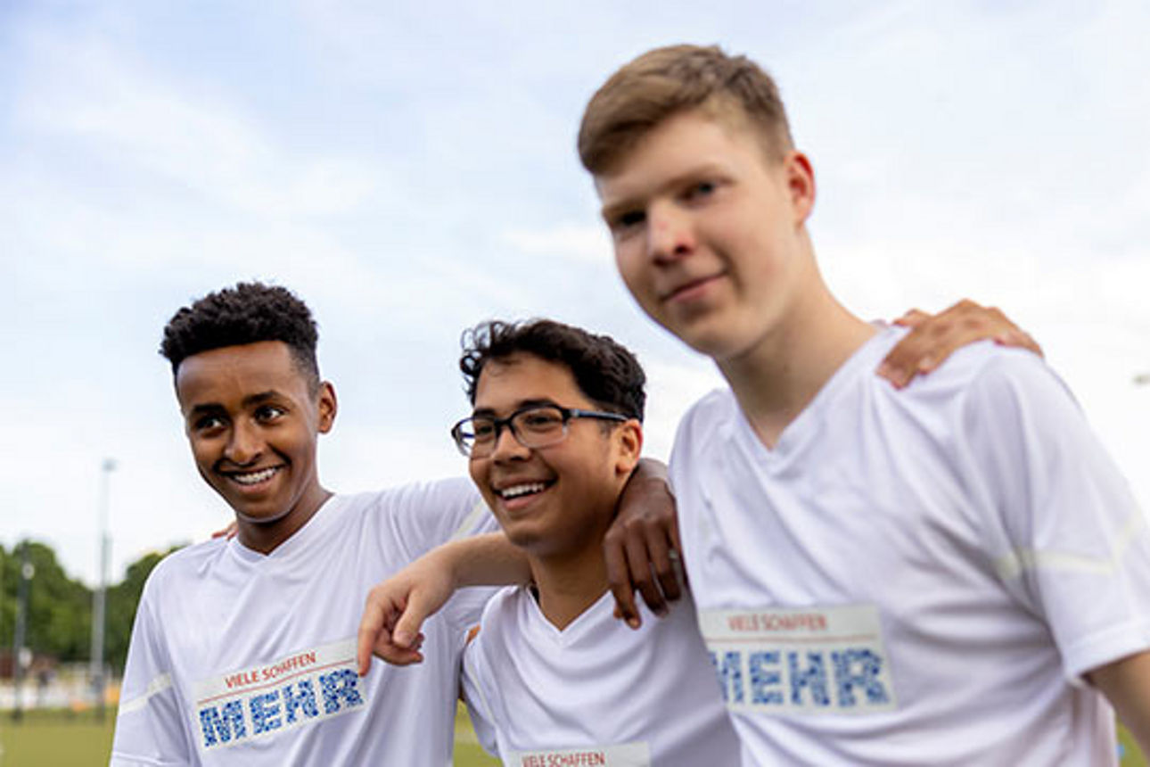 Drei Jungs in Fußballtrikots stehen Arm in Arm und lächeln