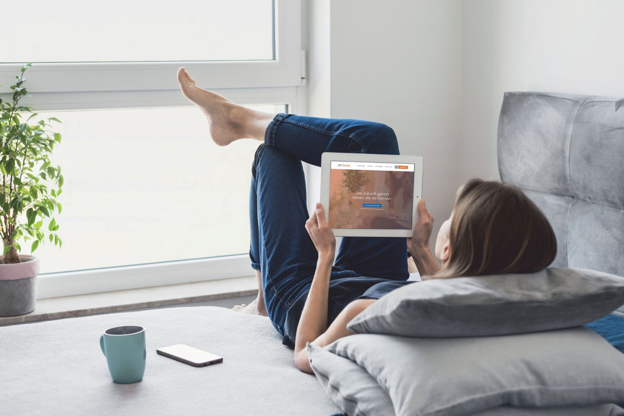 Junge Frau liegt auf dem Sofa, auf dem Tablet ist die Website VR-Crowd geöffnet.