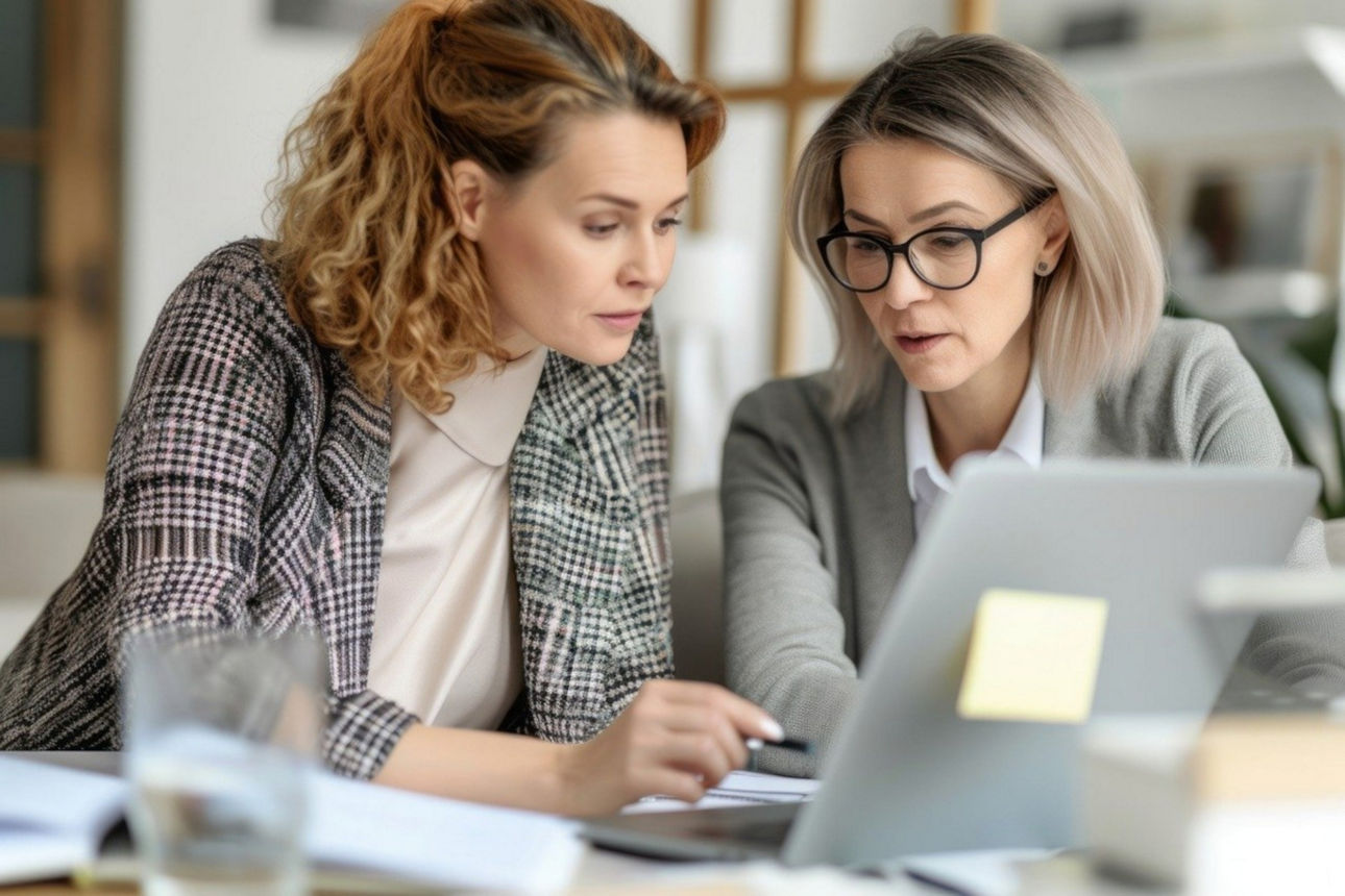 Zwei Geschäftsfrauen sitzen am Schreibtisch und studieren Unterlagen.