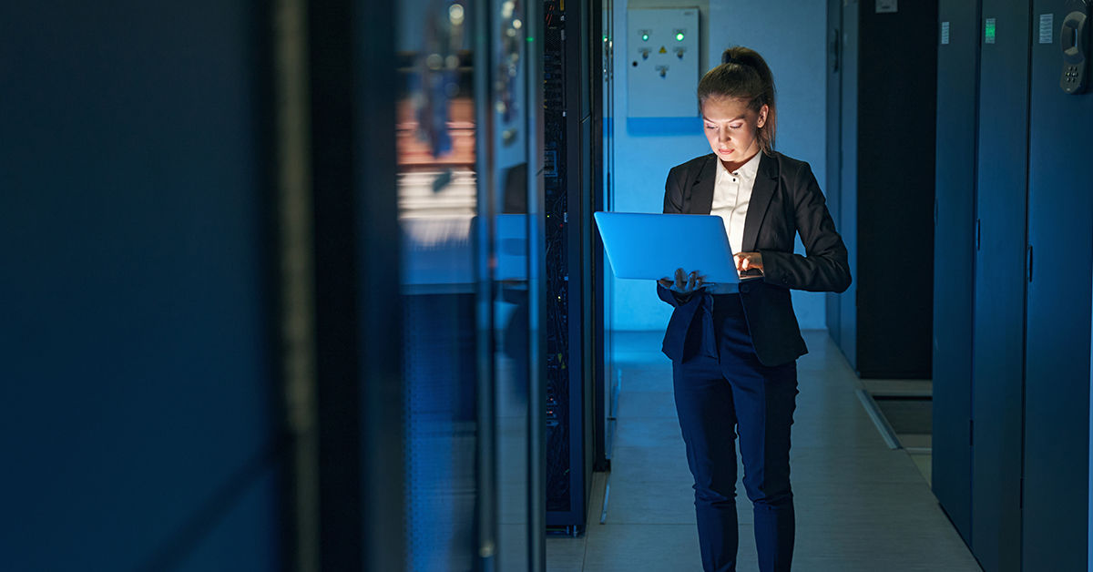 Frau in einem Serverraumblickt besorgt auf einen Laptop