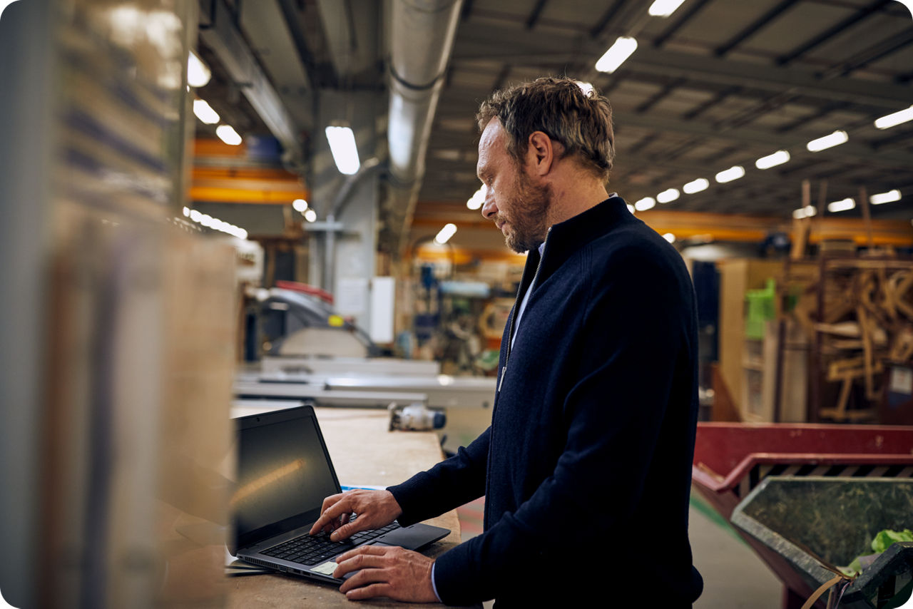 Ein Mann steht an einer Werkbank und arbeitet auf einem Laptop
