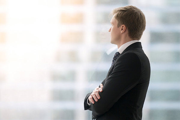 Ein Geschäftsmann steht mit verschränkten Armen vor einer Fensterfront