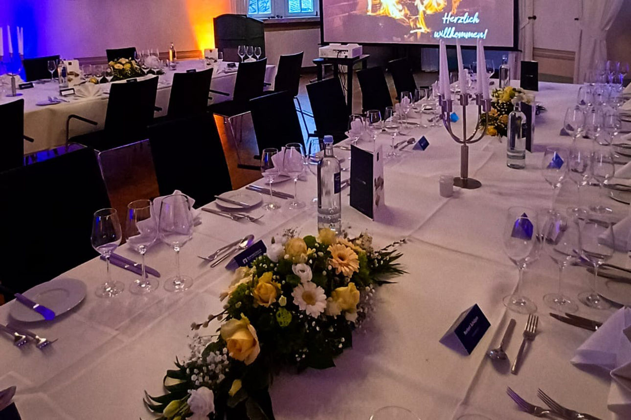 Eine gedeckte Tafel in einem eleganten Raum mit großen Fenstern und Kronleuchtern.