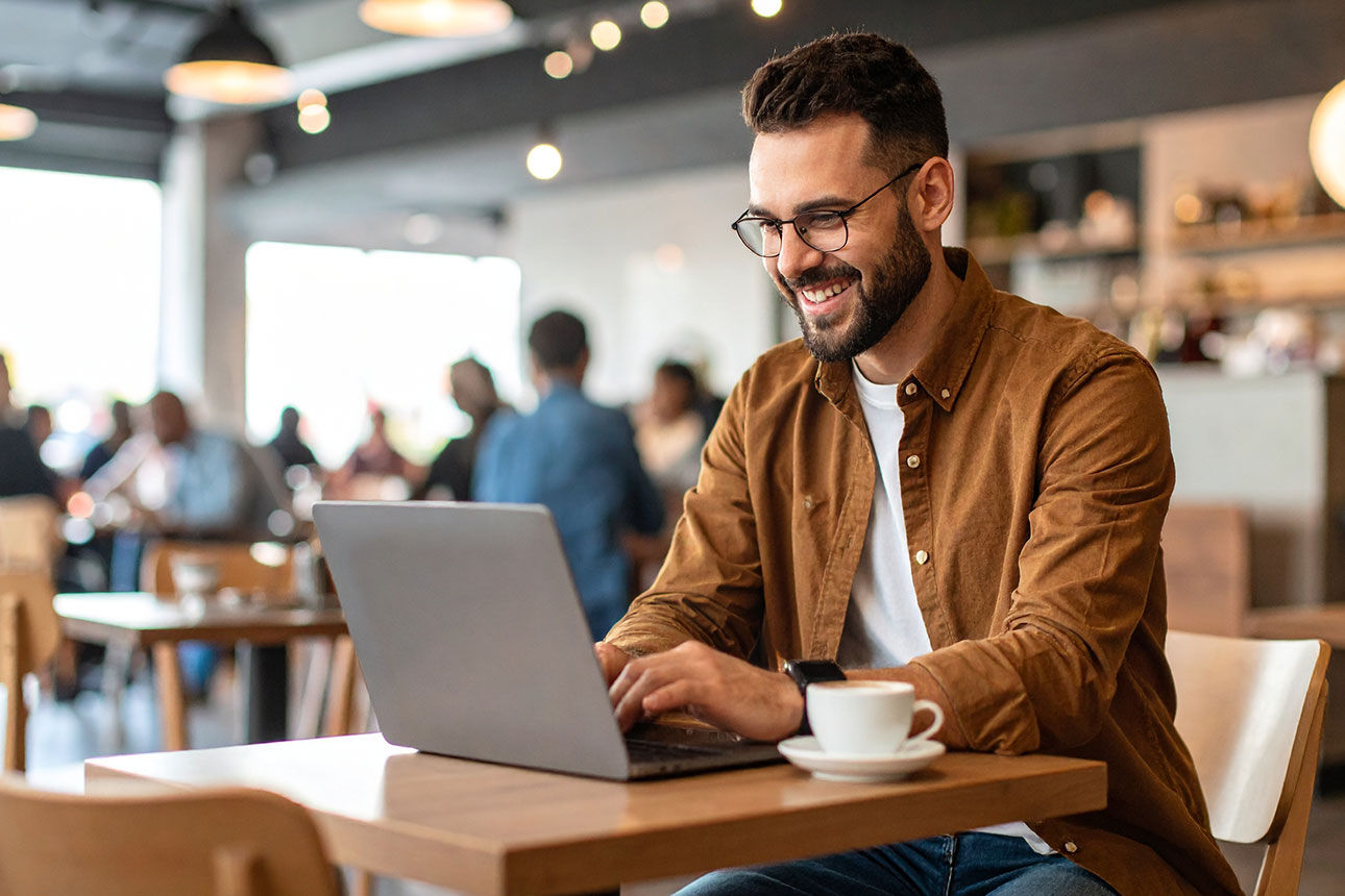Mann sitzt lächelnd vor einem Laptop. 