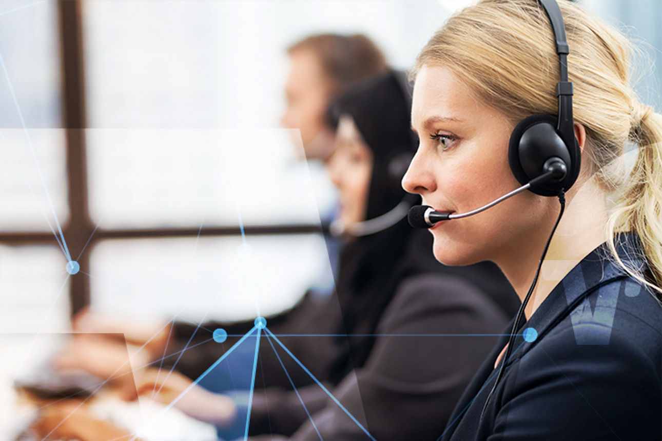 Eine Frau in einem schwarzen Blazer und mit Headset sitzt in einem Callcenter