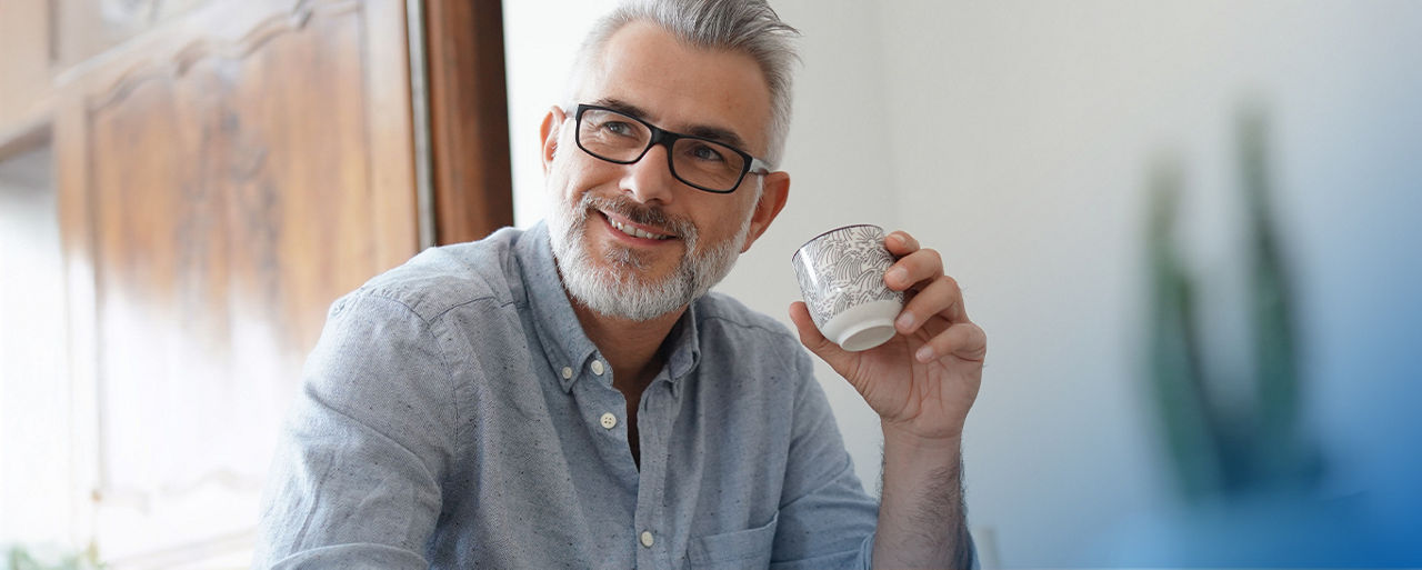 Ein Mann sitzt lächelnd da mit einer Tasse Kaffee in der Hand