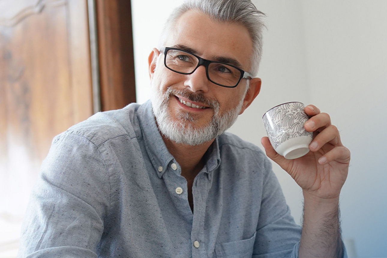 Ein Mann sitzt lächelnd da mit einer Tasse Kaffee in der Hand