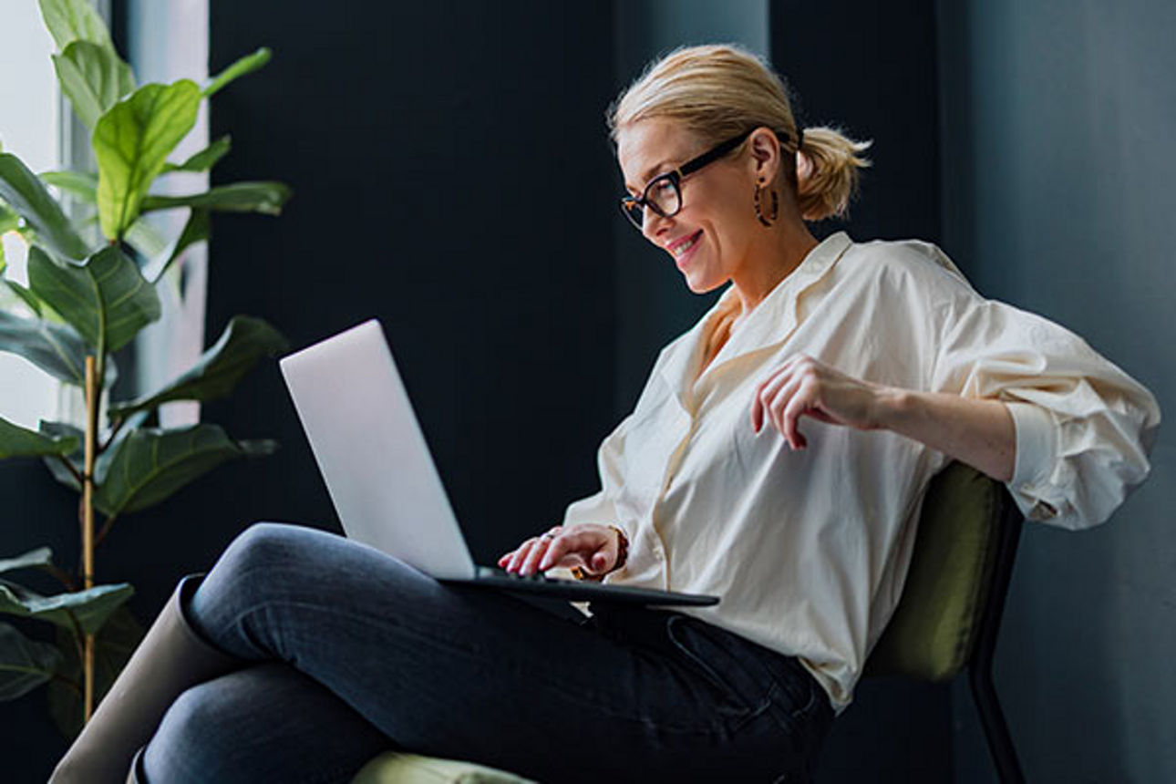 Frau sitzt mit ihrem Laptop auf einem Stuhl