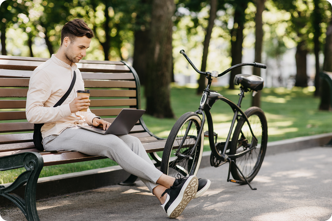 Ein junger Mann mit Fahrrad sitzt auf einer Parkbank mit seinem Notebook