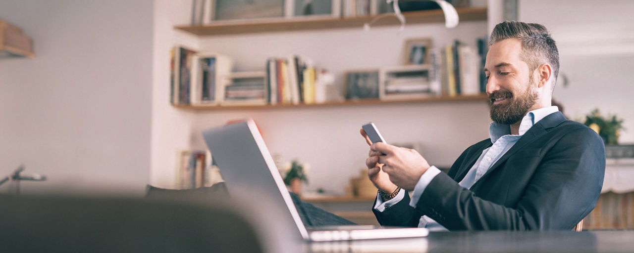 Mann sitzt am Tisch und eröffnet auf seinem Smartphone ein Online-Depot
