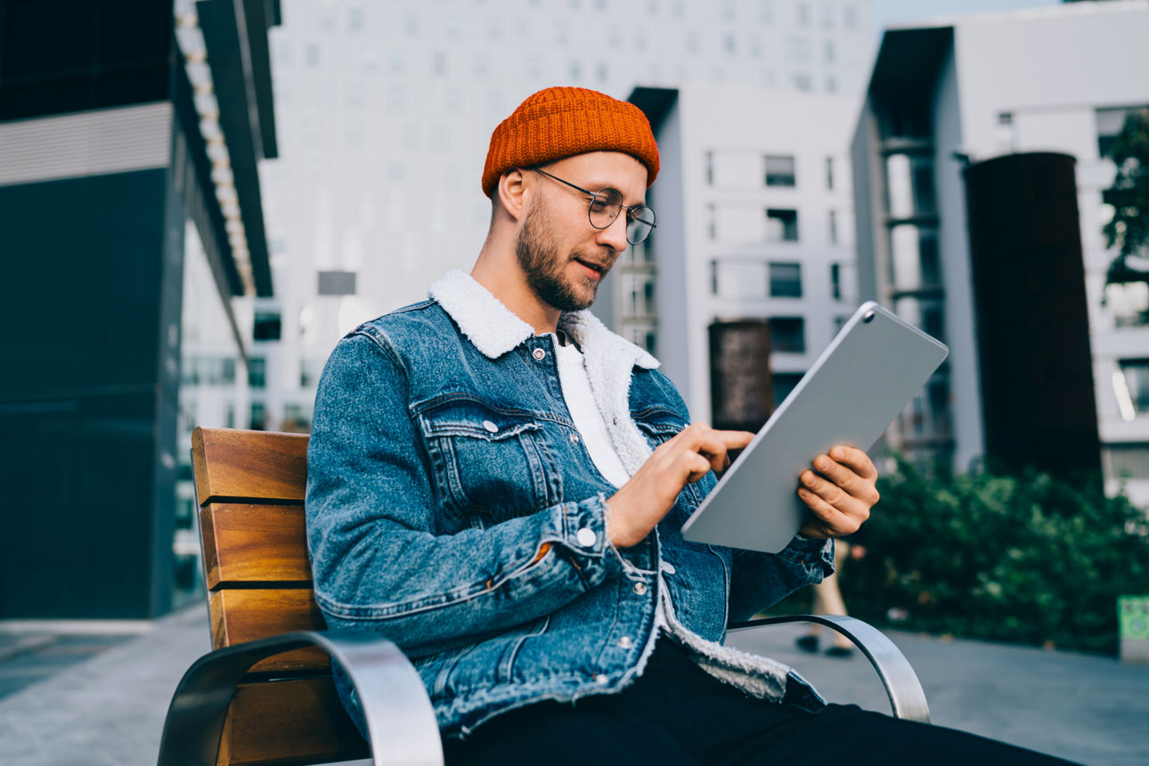 Der neue Schufa-Score 2026: So funktioniert das Bonitätsrating Mann sitzt auf Bank und nutzt ein Tablet im Freien.